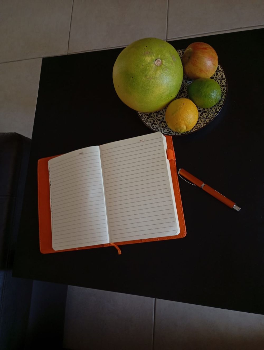 The notebook open on a dark table beside a bowl of citrus fruit in Larnaca