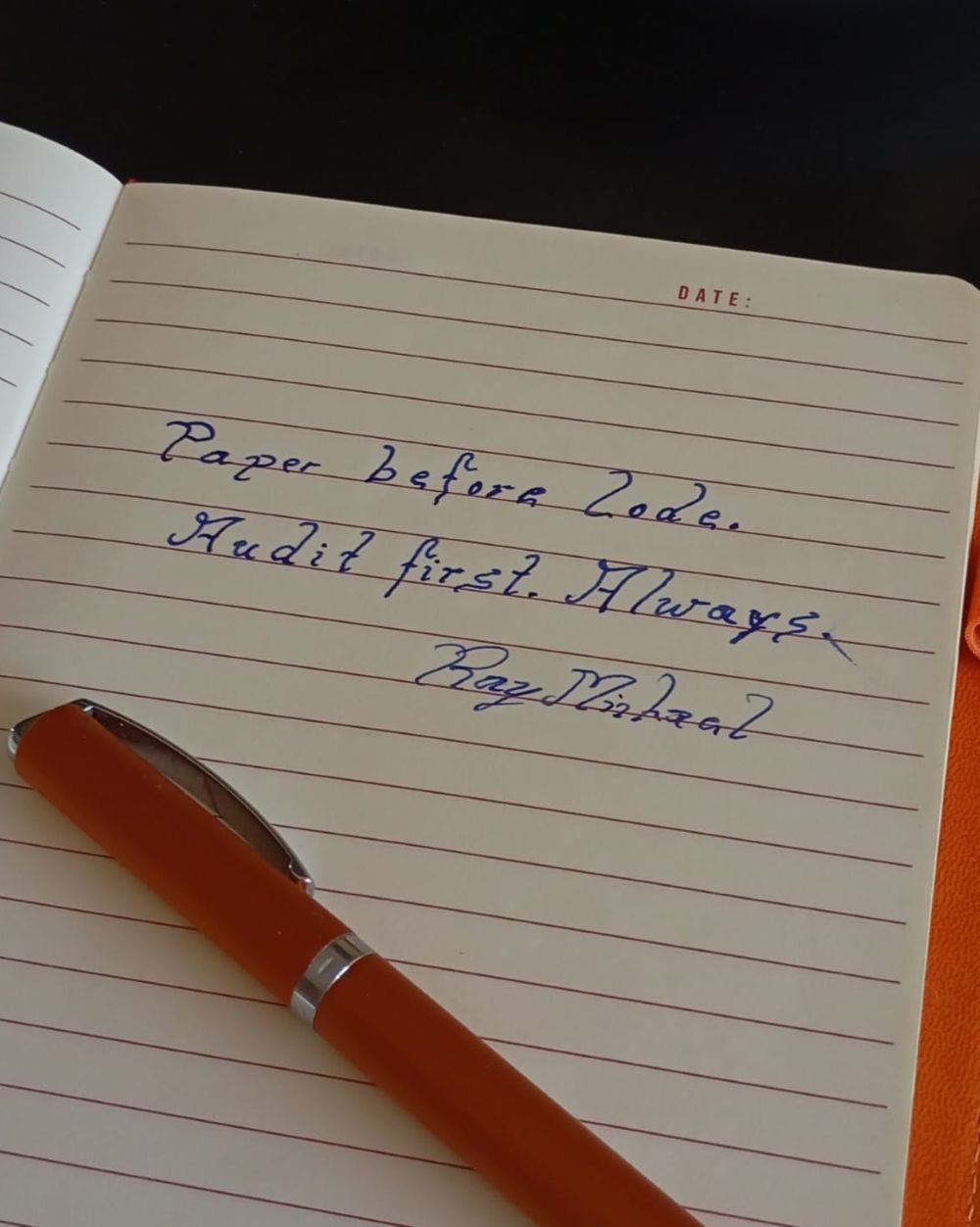 The same notebook page seen from an angle, orange pen resting on the ruled paper